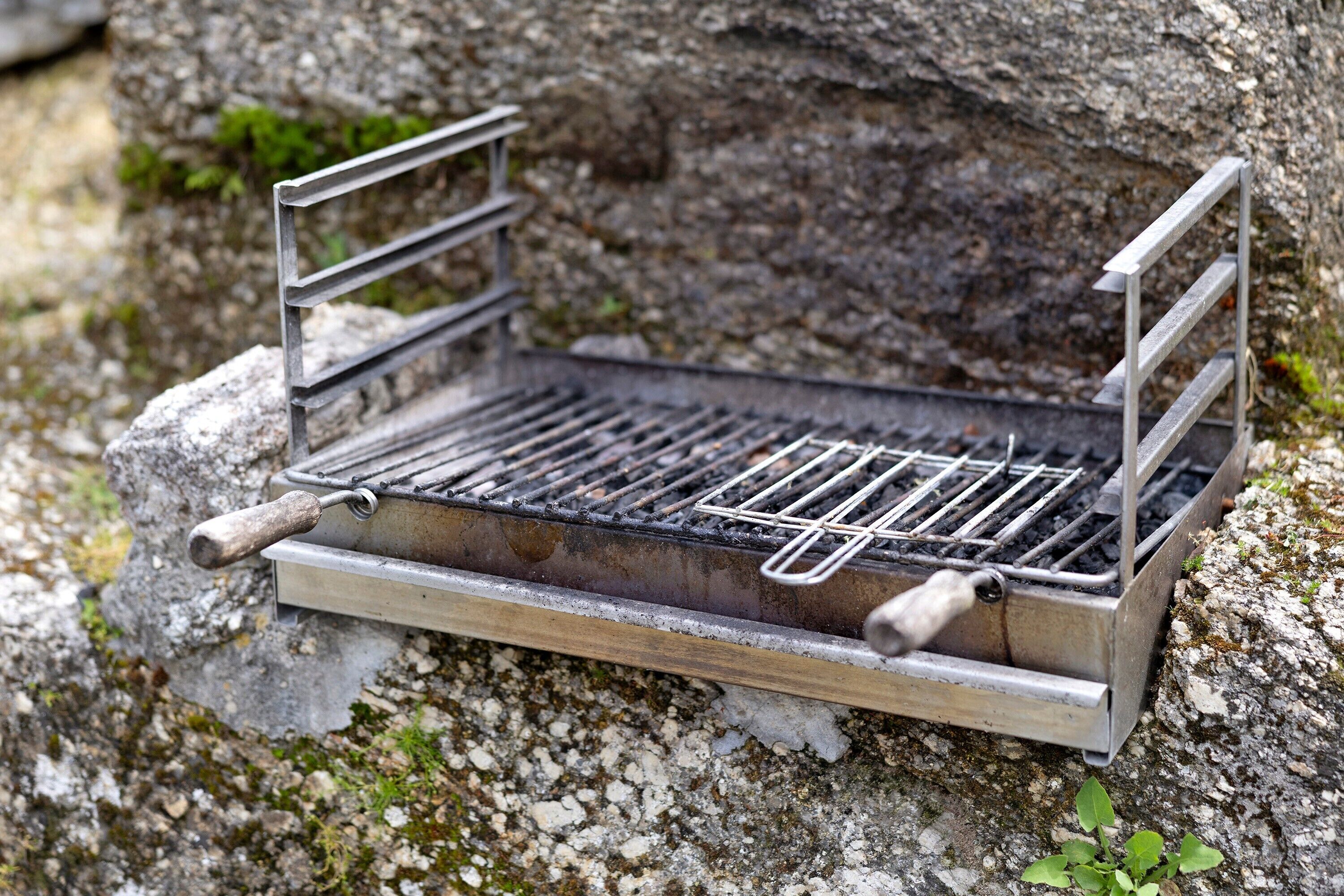 A portable grill with a metal frame and a flat grate, placed on a rocky surface.