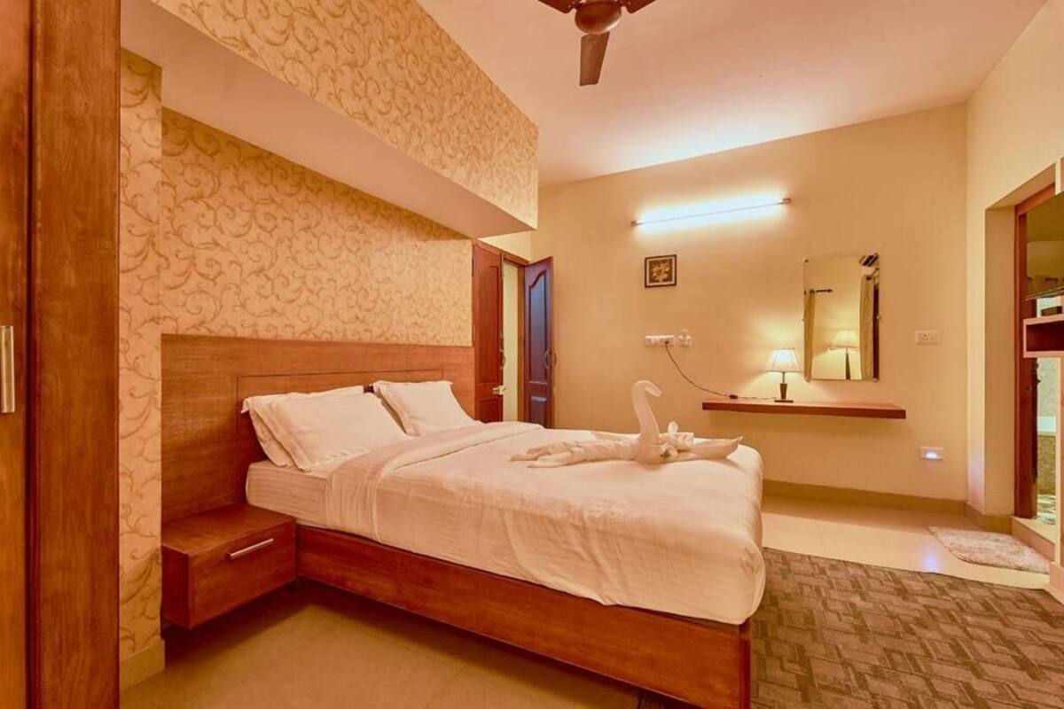 A hotel room with a wooden bed, a nightstand, a wall-mounted shelf, a ceiling fan, and a patterned wallpaper.