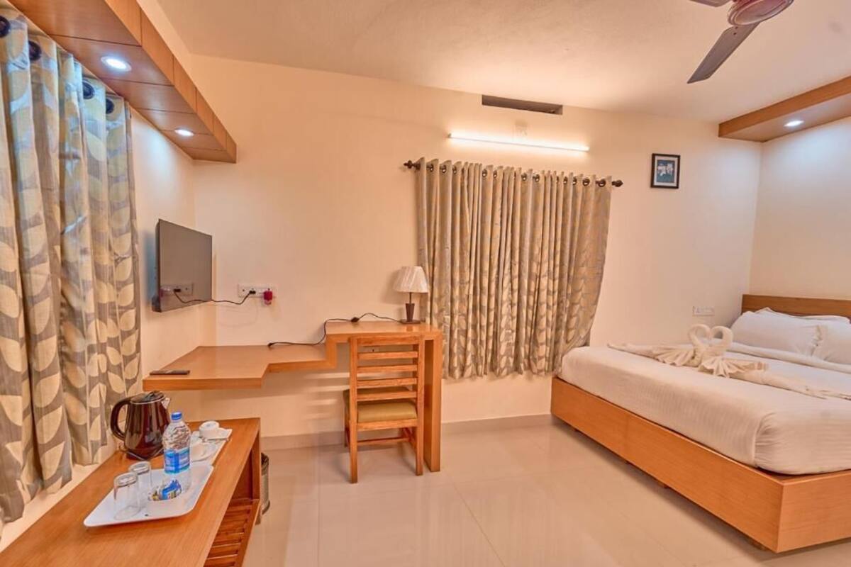 A hotel room with a bed, a desk with a chair, a television, and a window with curtains.