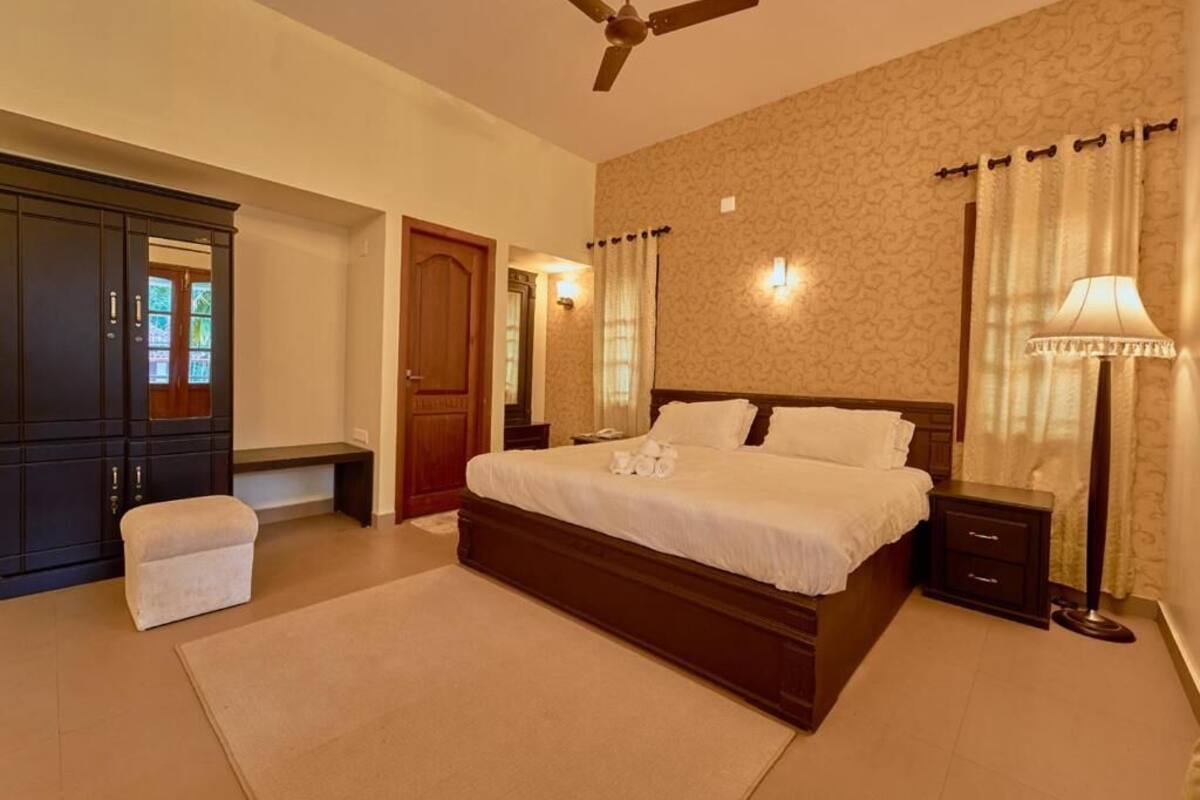 A bedroom with a large bed, a ceiling fan, a nightstand, a lamp, and a wardrobe.
