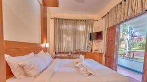 A hotel room with a bed, a TV, a wooden headboard, a window with curtains, and a view of the outside. - Ushasree Wayanad Resort by VOYE HOMES (Sulthan Bathery)