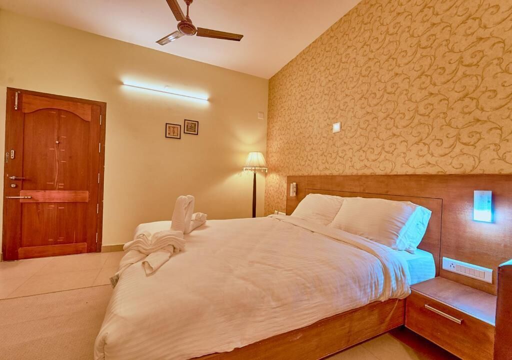 A hotel room with a wooden bed, a nightstand, a wall-mounted light, a ceiling fan, and a door.
