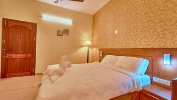 A hotel room with a wooden bed, a nightstand, a wall-mounted light, a ceiling fan, and a door.