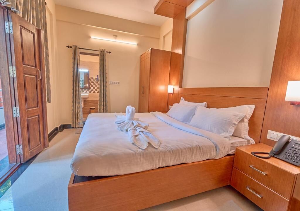 Une chambre d’hôtel avec un lit en bois, un téléphone sur la table de chevet et un miroir.