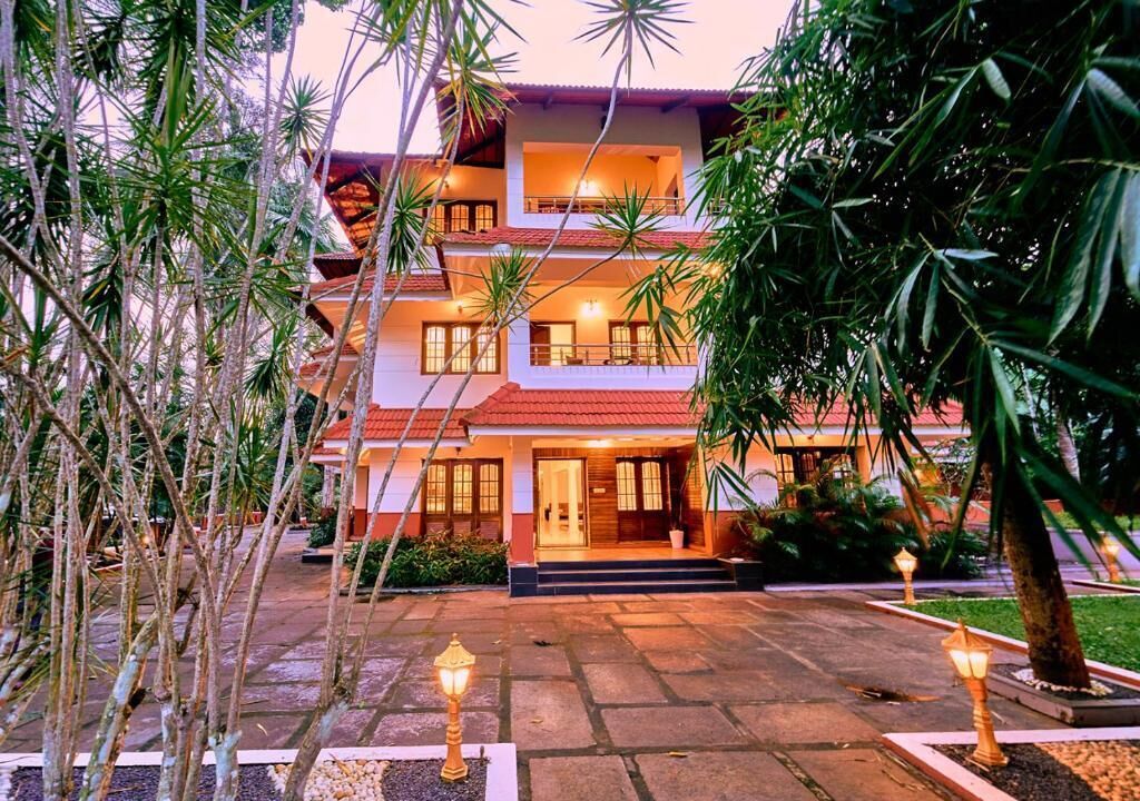 A multi-story hotel with a red-tiled roof, a well-lit entrance, and a landscaped courtyard with pathways and lamp posts.
