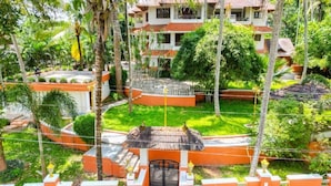 A two-story building with a red-tiled roof, surrounded by lush greenery and palm trees. - Ushasree Wayanad Resort by VOYE HOMES (Sulthan Bathery)