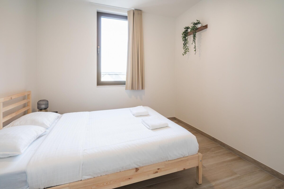 Una cama individual con estructura de madera, ropa de cama blanca y una ventana con cortinas.