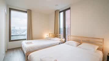 Een hotelkamer met twee bedden, een groot raam met uitzicht over de stad en een balkon.