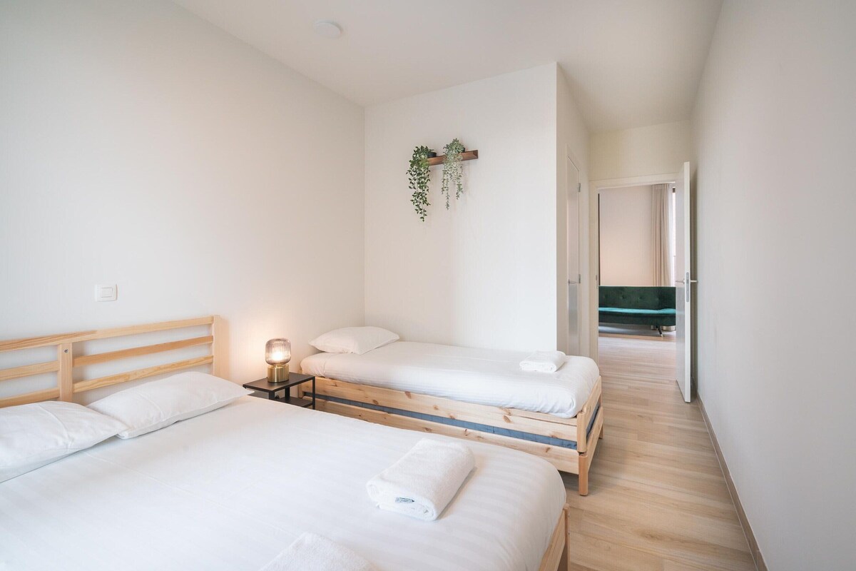 Un dormitorio con dos camas, una mesita de noche con lámpara y una planta colgante.