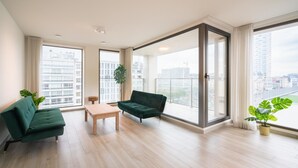 Un amplio salón con un sofá, una mesita y grandes ventanales con vistas a la ciudad.