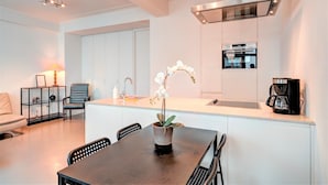 A modern kitchen with a dining area, white cabinetry, a coffee machine, and a potted orchid.