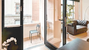 A modern living room with a glass door leading to a balcony, a leather sofa, a dining table, and a potted plant.
