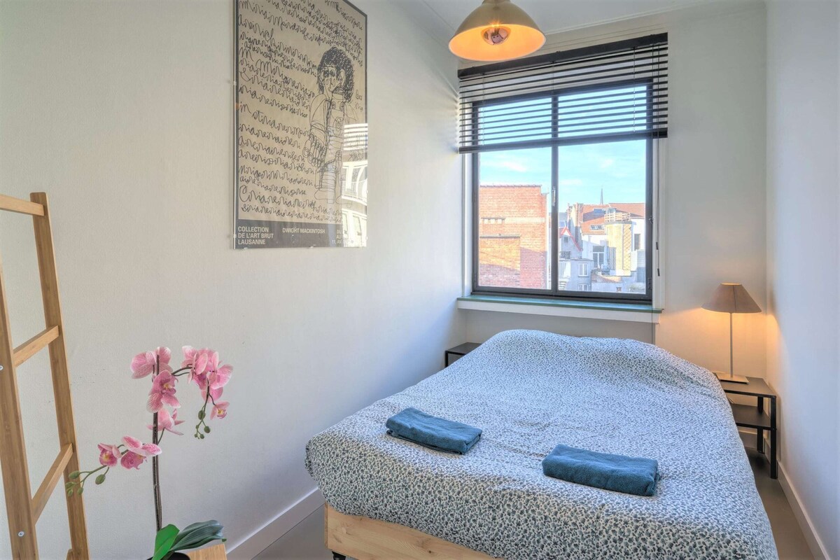 A bedroom with a bed, a window with blinds, a lamp, and a poster on the wall.