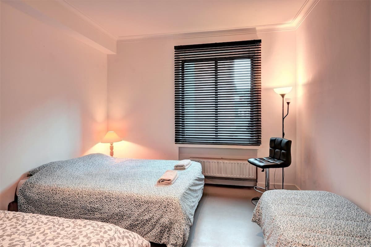 Un dormitorio con dos camas, un radiador, un escritorio con silla y una ventana con persianas.
