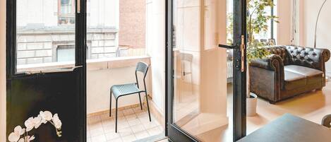 Un apartamento moderno con balcón, un sofá de cuero, una mesa de comedor y una planta en maceta.