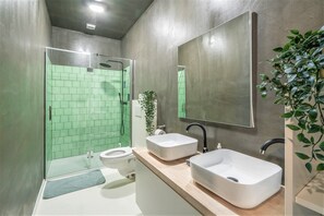 Ein modernes Badezimmer mit Duschkabine aus Glas, zwei Waschbecken, einer Toilette und einem großen Spiegel.