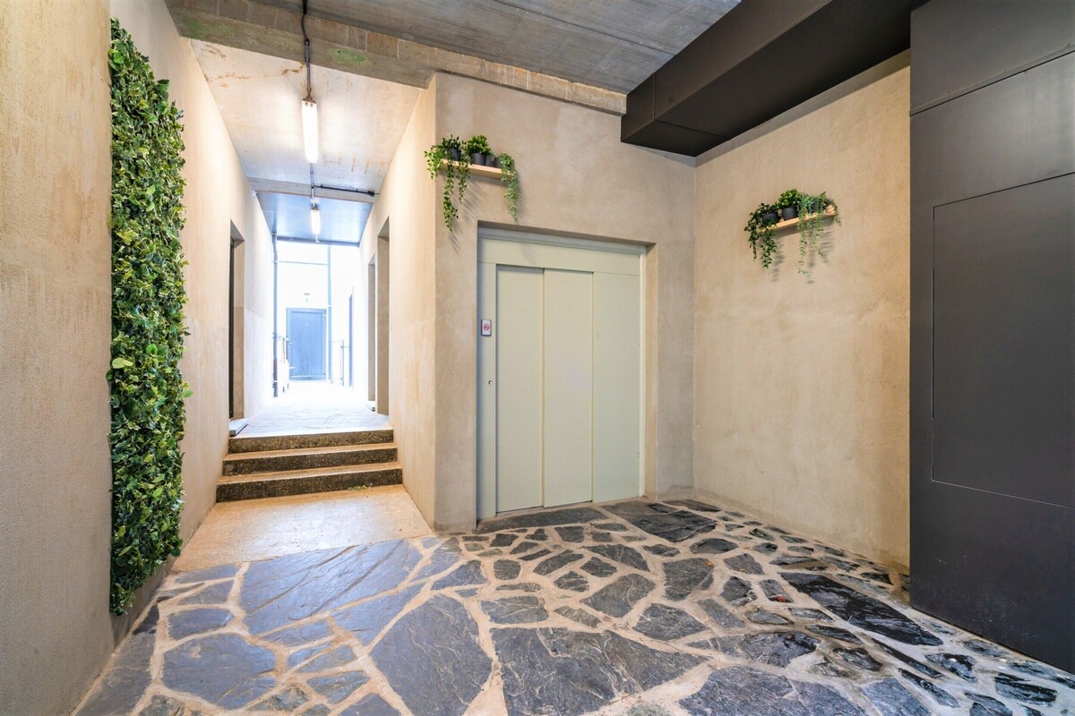 A hallway with a stone floor, a light blue door, and green plants on the walls.