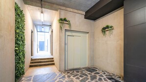 Un passadís amb sòl de pedra, una porta de blau clar i plantes verdes a les parets.