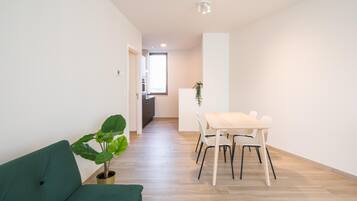 Uma sala de estar moderna com um sofá verde, uma mesa de jantar com cadeiras e um vaso de planta.