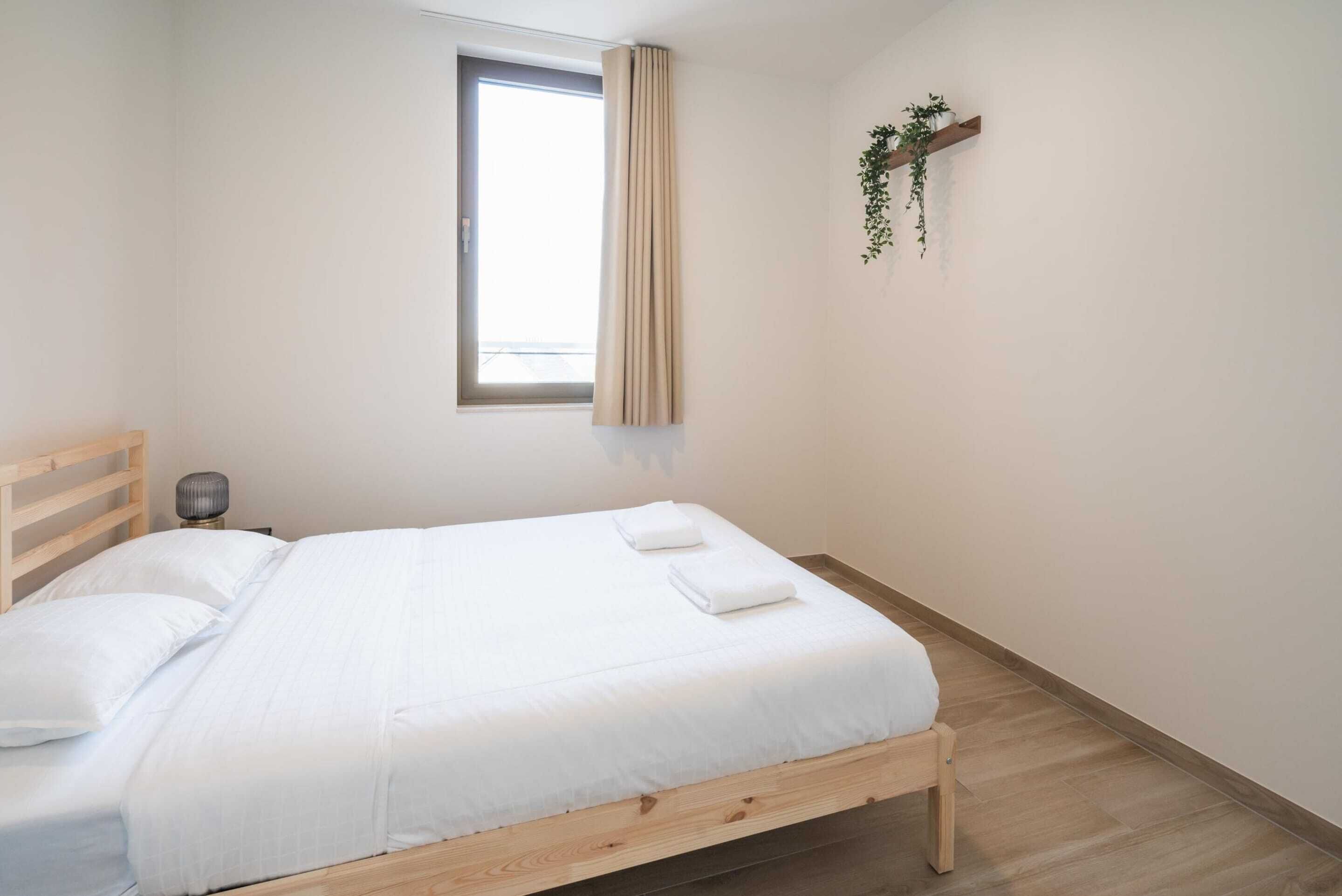 Een eenpersoonsbed met houten frame, witte beddengoed en een raam met gordijnen.