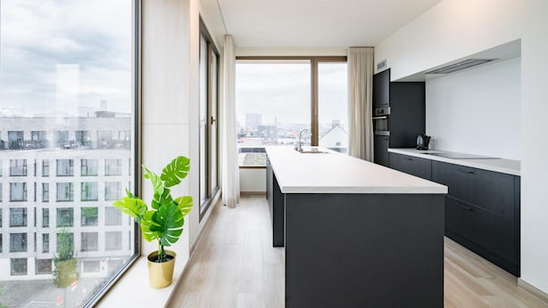 Una cocina moderna con una isla grande, armarios oscuros y vistas a la ciudad a través de amplios ventanales.
