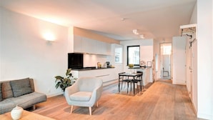 A modern living room with a sofa, armchair, and coffee table, a kitchen area with cabinets and a TV, and a dining area with chairs and a table. - Lighthouse Apartment in Heart of Antwerp (Antwerp)