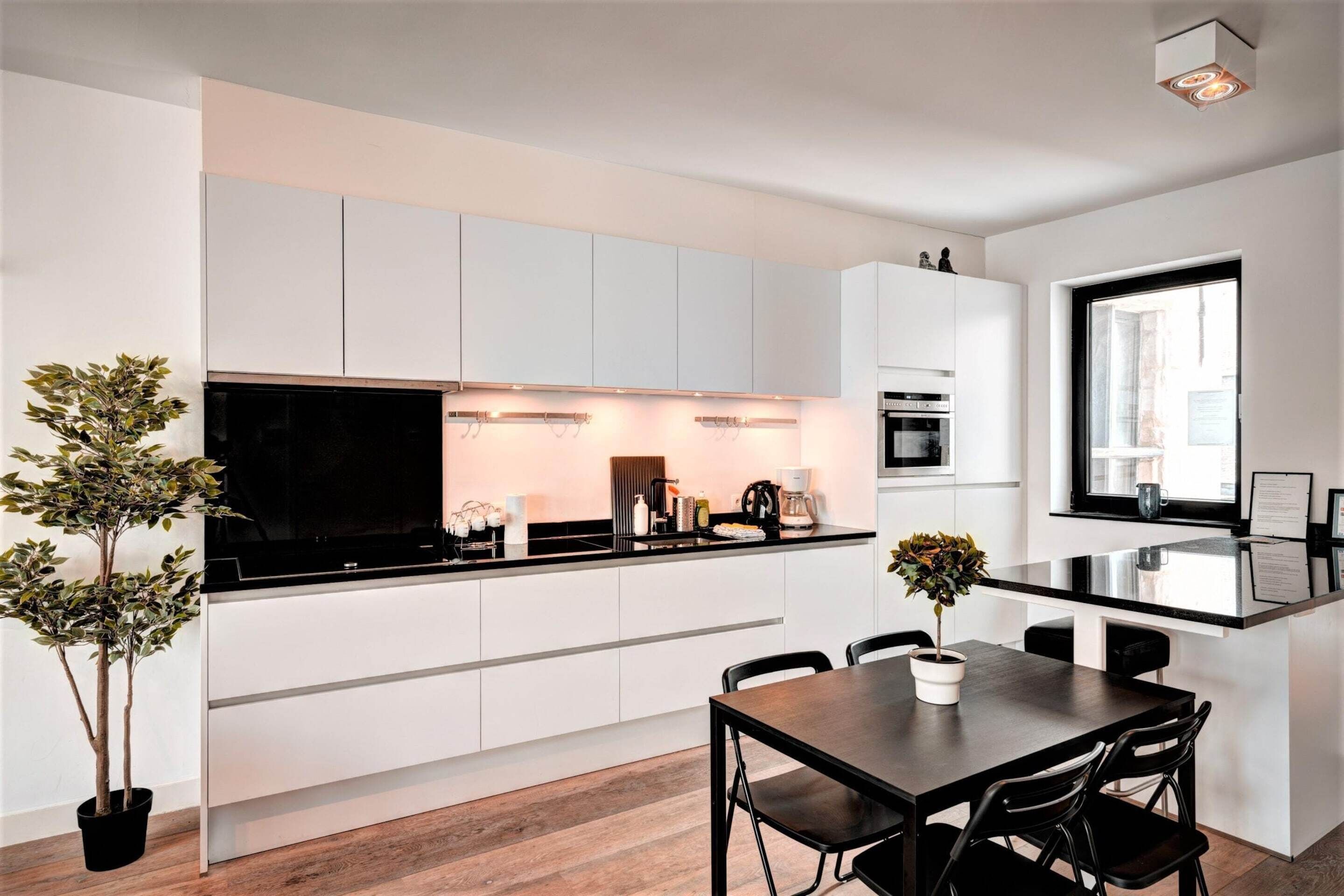 Een moderne keuken met witte kastjes, een zwart aanrecht en een eethoek met een tafel en stoelen.