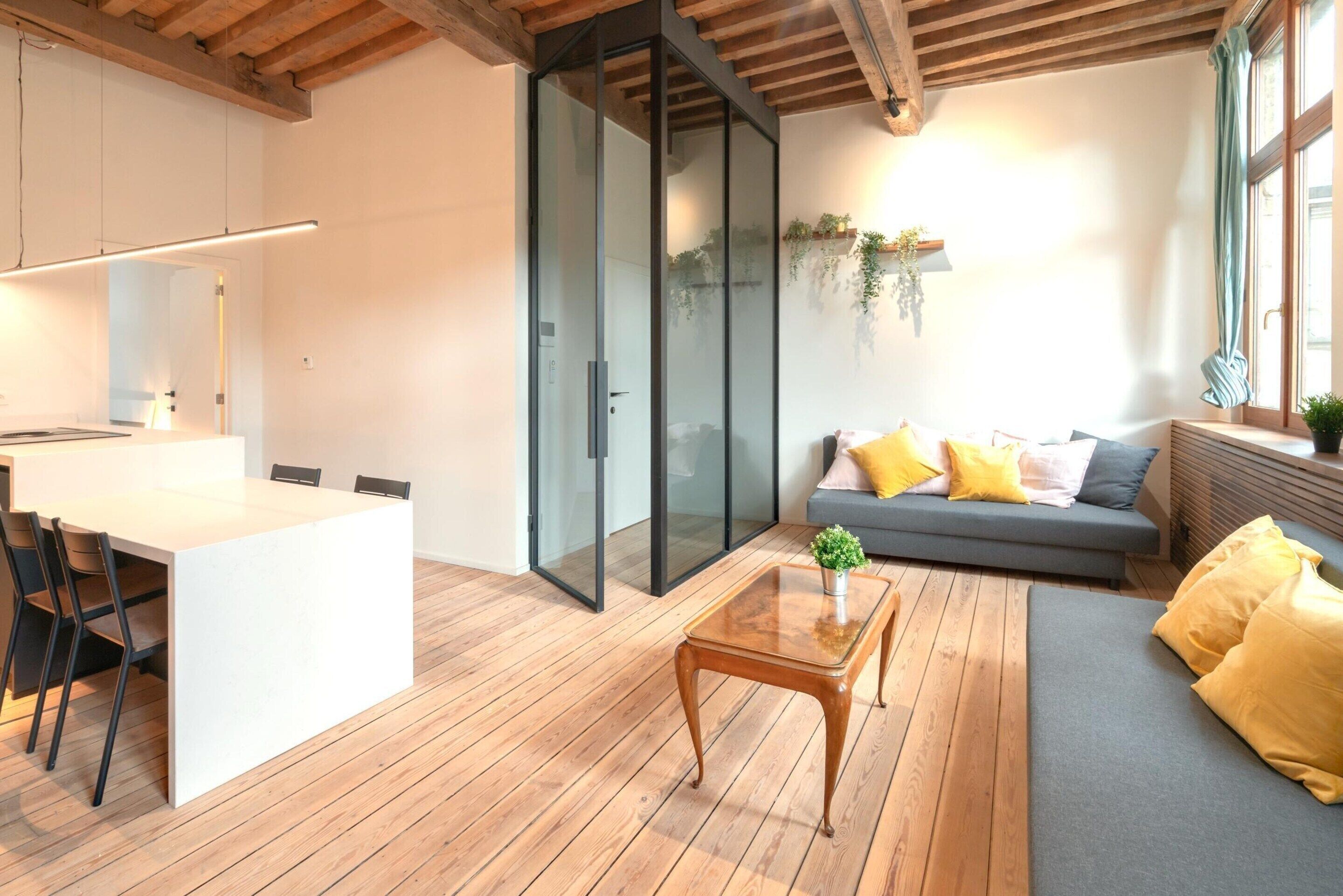 Ein moderner Wohnraum mit Essbereich, einer Couch mit Kissen, einem Couchtisch und einer Glasschiebetür, die auf einen Balkon führt.