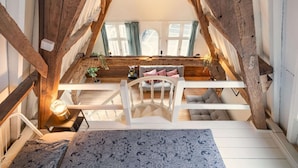 Un dormitorio tipo loft con escalera de madera, cama blanca y vista al área de estar.