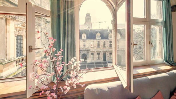 Una habitación con un ventanal grande, un florero con flores y vistas a edificios.