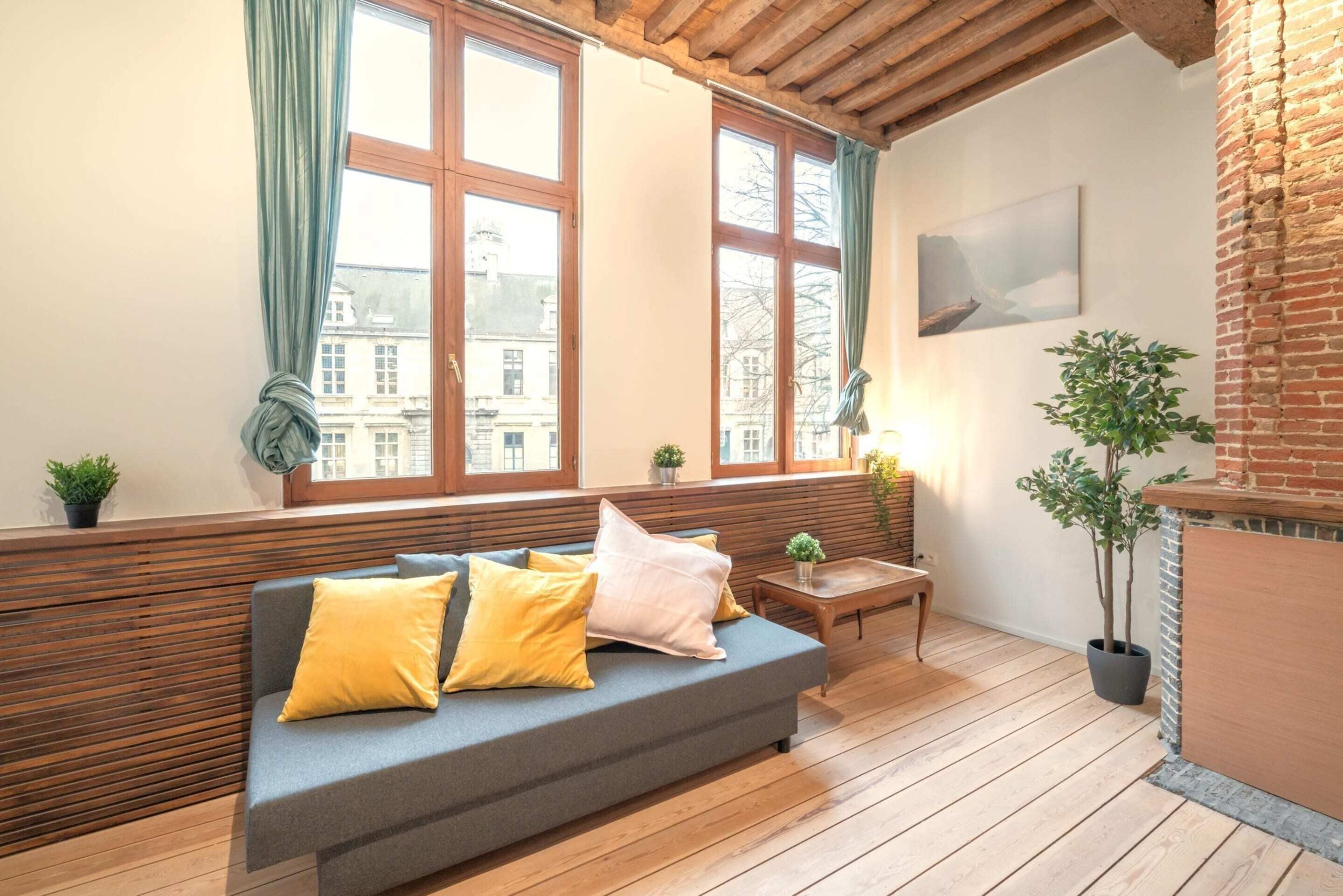 Ein gemütlicher Raum mit einer Holzbank, einer Couch mit Kissen, einem kleinen Tisch und einem Blumentopf.