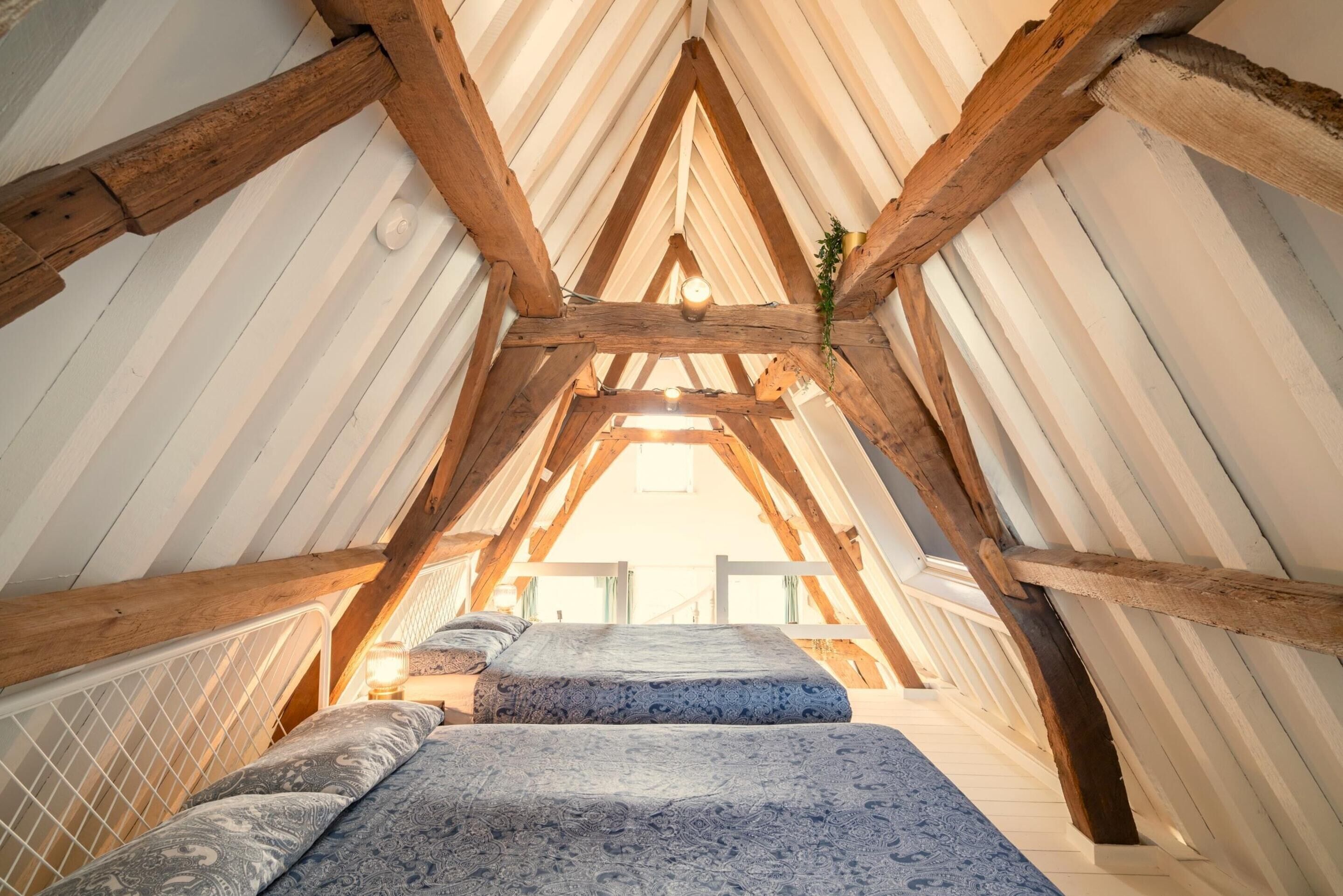 An attic bedroom with a sloped ceiling, wooden beams, and a bed with patterned bedding.