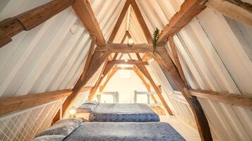 An attic bedroom with a sloped ceiling, wooden beams, and a bed with patterned bedding.
