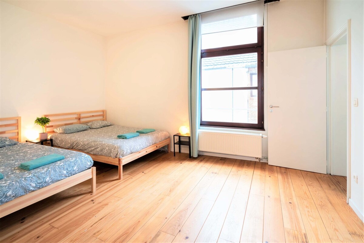 A bedroom with two beds, a window, a radiator, and a door.