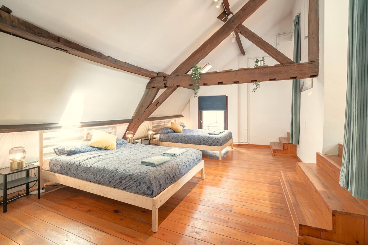 Une chambre avec deux lits, des poutres en bois, un escalier et une fenêtre.