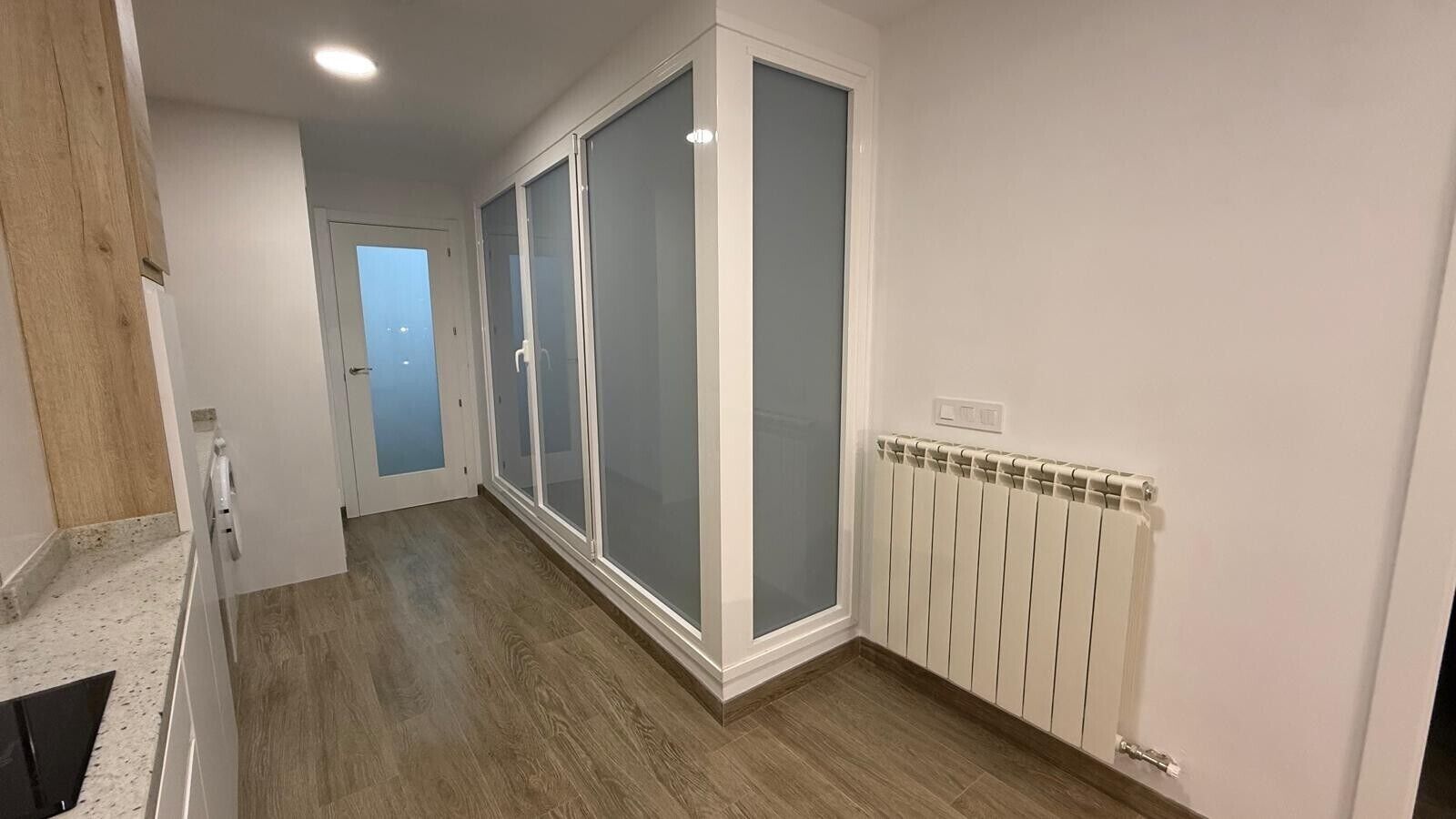 A hallway with a wooden floor, a white radiator, and a door leading to another room.