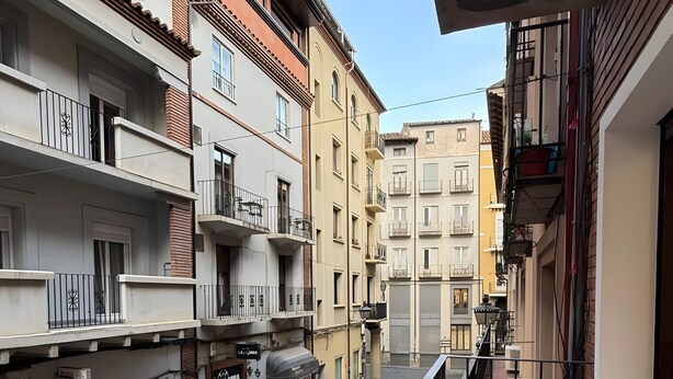 A residential building with multiple balconies, a tiled terrace, and a street view.