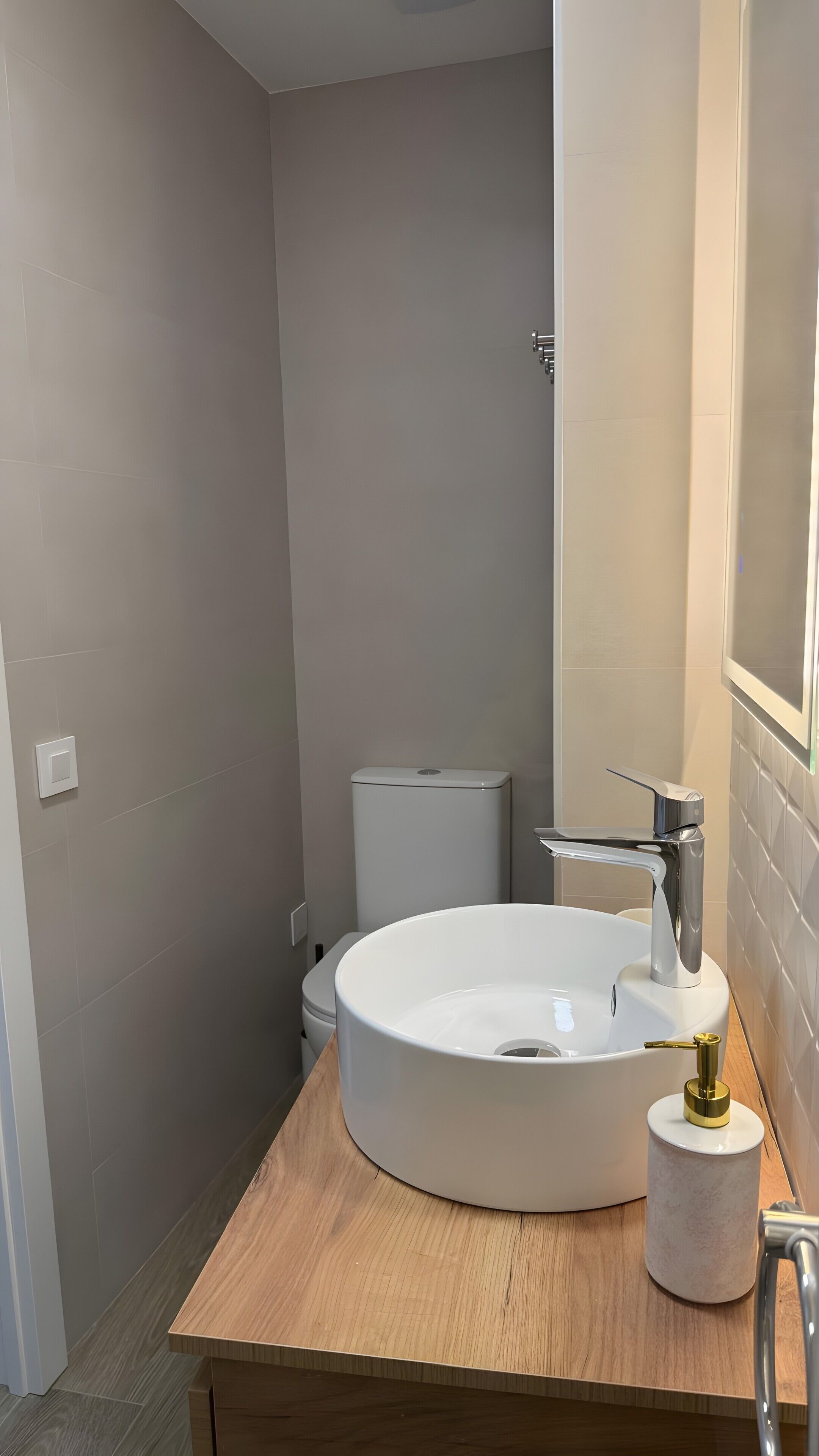 Un bagno con un lavandino bianco tondo, un water e uno specchio.
