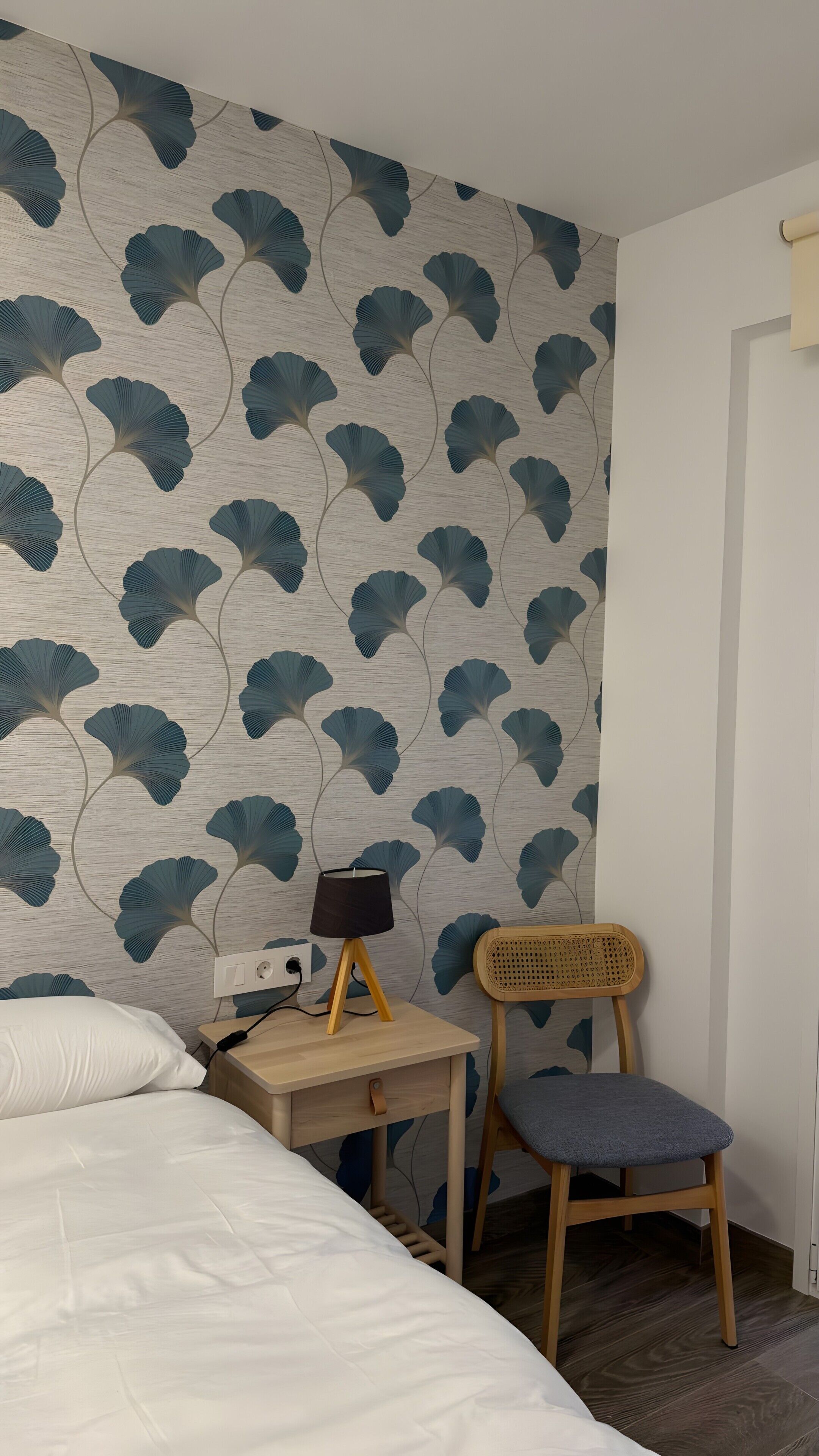 Un dormitorio con cama, un escritorio con lámpara, una silla y una pared con diseño de hojas.