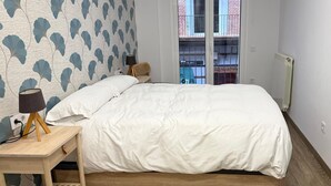 A bedroom with a bed, bedside tables, and a view of a building through a window.