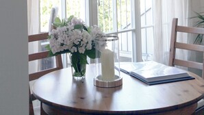 Una habitación con un gran ventanal, una mesa con un jarrón de flores, una vela y un libro.