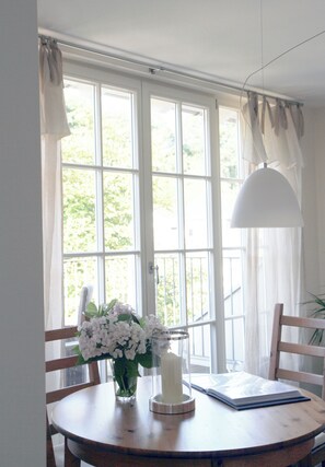 A room with a large window, a table with a vase of flowers, a candle, and a book.