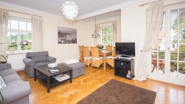 Sala de estar com sofá, mesa de centro, televisão, mesa de jantar, cadeiras e lustre.