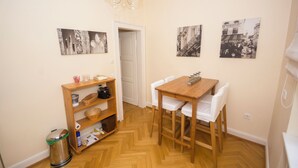 Uma pequena área de refeições com uma mesa e cadeiras de madeira, uma estante e um cesto de lixo.