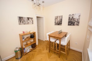 Un pequeño comedor con una mesa y sillas de madera, una estantería y un cubo de basura.