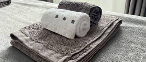 A neatly folded set of towels on a bed with a headboard and curtains in the background.