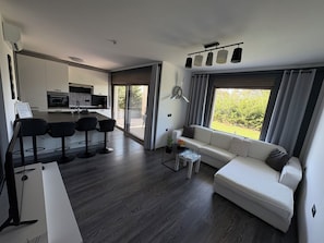 A modern living space with a kitchen, dining area, and a sofa by a large window. - Cozy family apartment in quiet surroundings close to the sea (Kostrena)