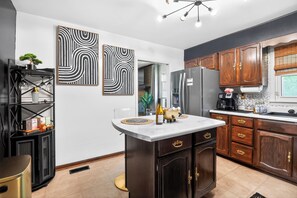 A modern kitchen with dark wood cabinets, a white countertop, and two abstract wall art pieces. - Boutique Family Retreat near Fort Eustis & Williamsburg (Newport News)