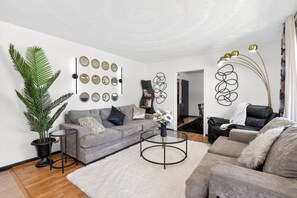 A modern living room with a grey sofa, a round coffee table, and a potted plant. - Boutique Family Retreat near Fort Eustis & Williamsburg (Newport News)