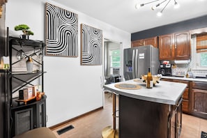 A modern kitchen with a central island, wooden cabinets, and abstract wall art.